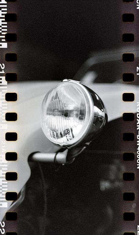 A close-up of a car headlight is visible with film borders on the left and right.