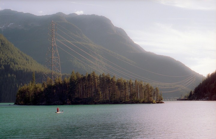 A person paddleboards on a lake with a forested island and mountains in the background.