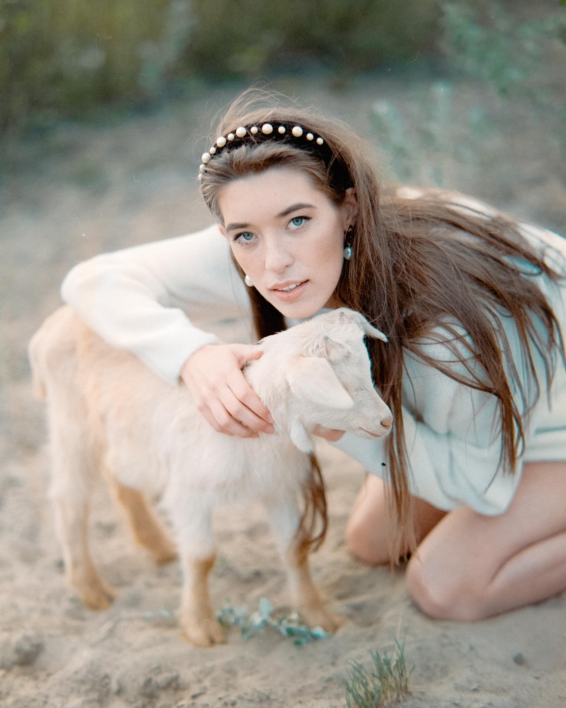 A woman kneels on the ground and embraces a small goat.