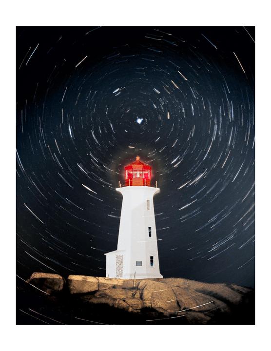 A white lighthouse with a red top stands on a rocky shore under a night sky filled with star trails.