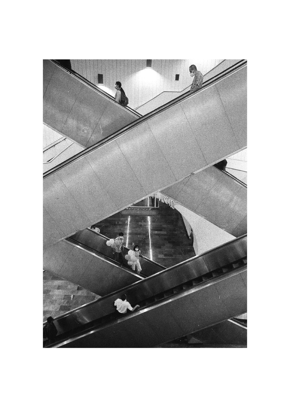 People ride multiple escalators that crisscross in a large building.