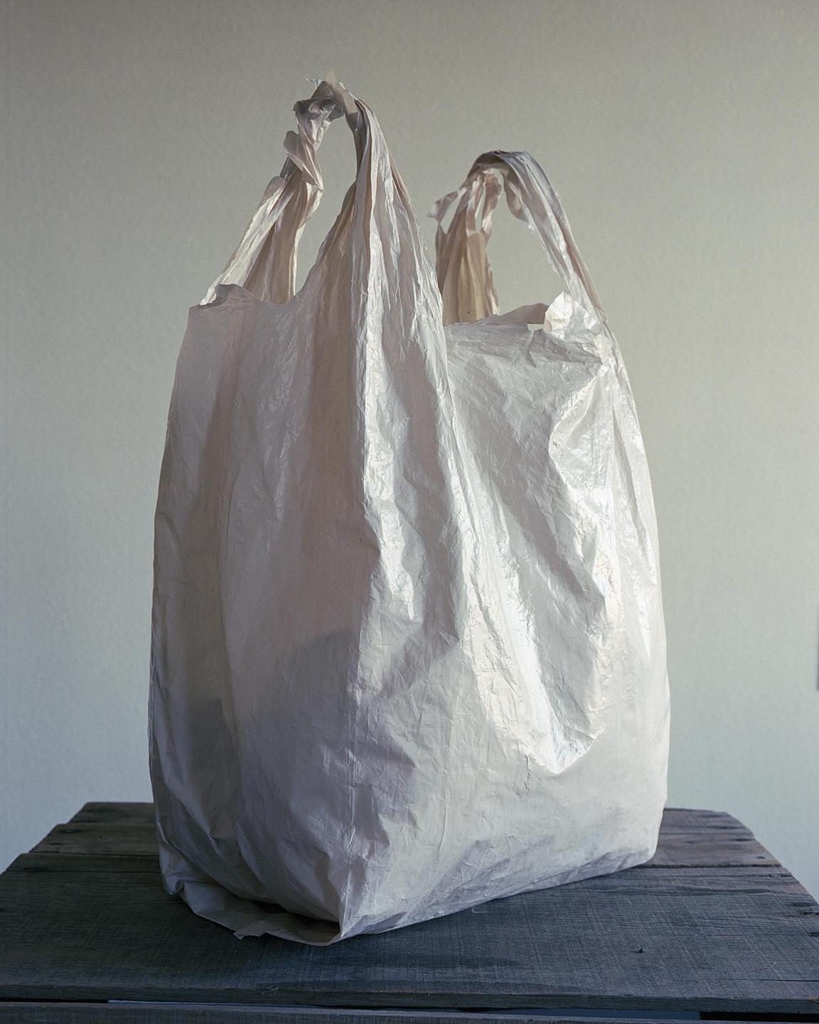 A white plastic bag sits on a wooden surface against a light background.