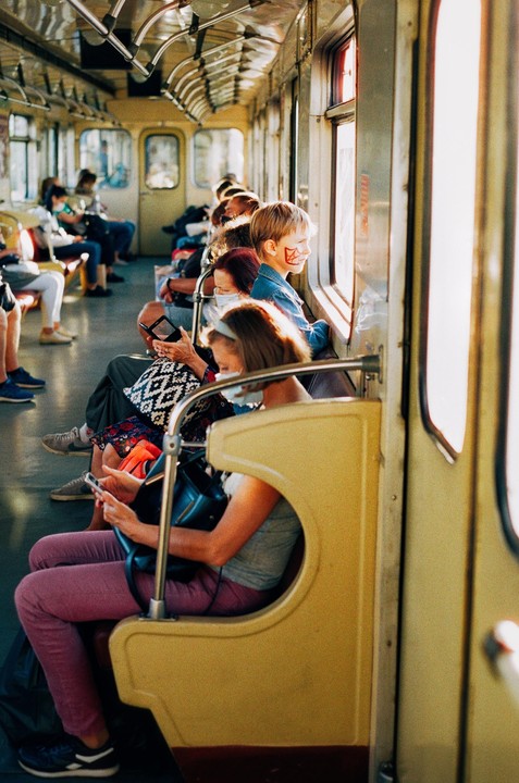 People sit inside a train car with sunlight streaming through the windows.