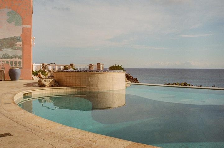 A swimming pool and hot tub overlook the ocean next to a building with a mural.