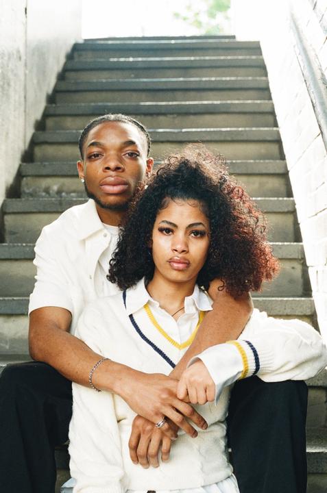 A couple sits on concrete steps, with the man embracing the woman from behind.