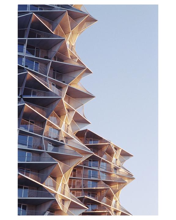 A modern building with a geometric facade and balconies is illuminated by sunlight.