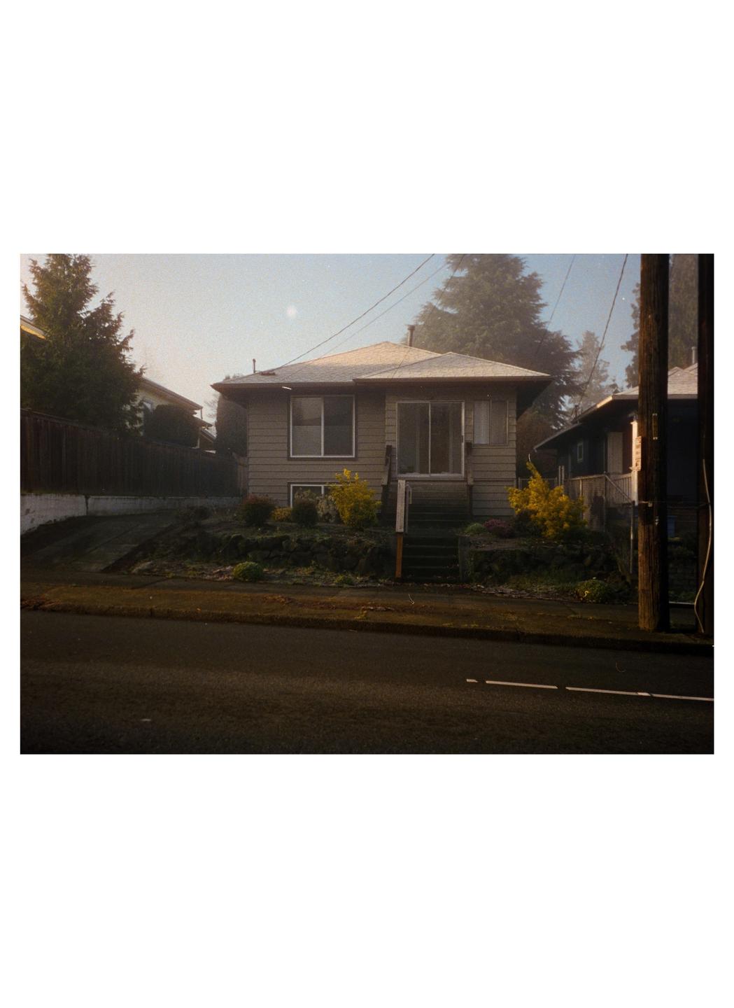 A house with a small front yard and steps leading to the entrance is seen from across the street.