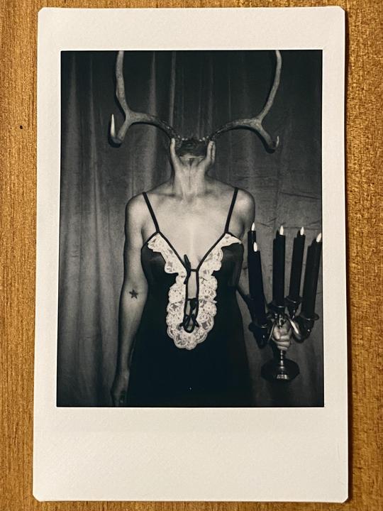 A woman with antlers for a head holds a candelabra with five lit candles.