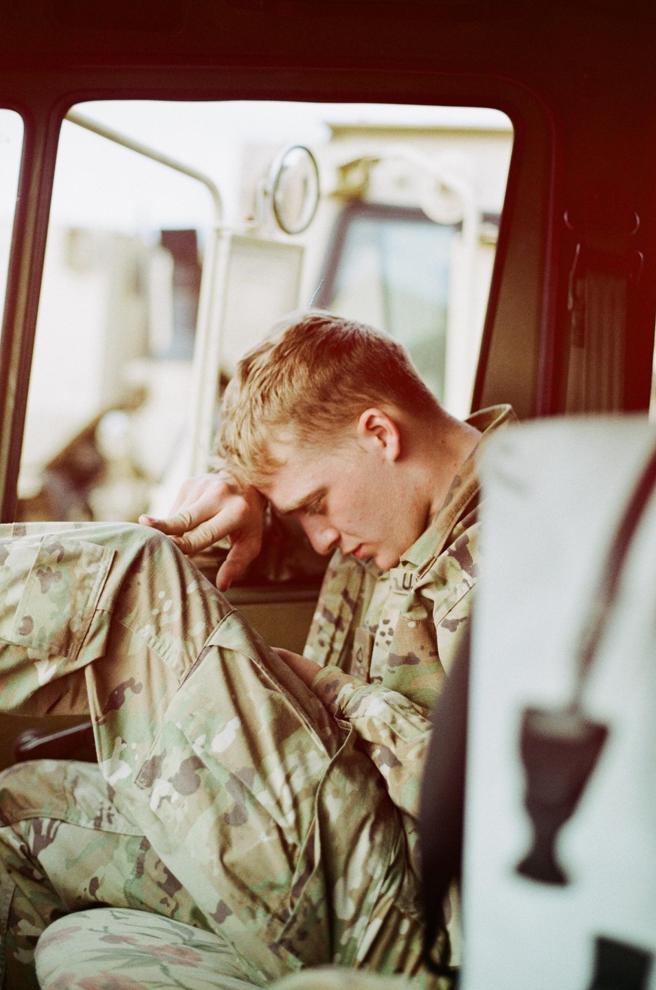 A man in camouflage uniform is resting inside a vehicle.
