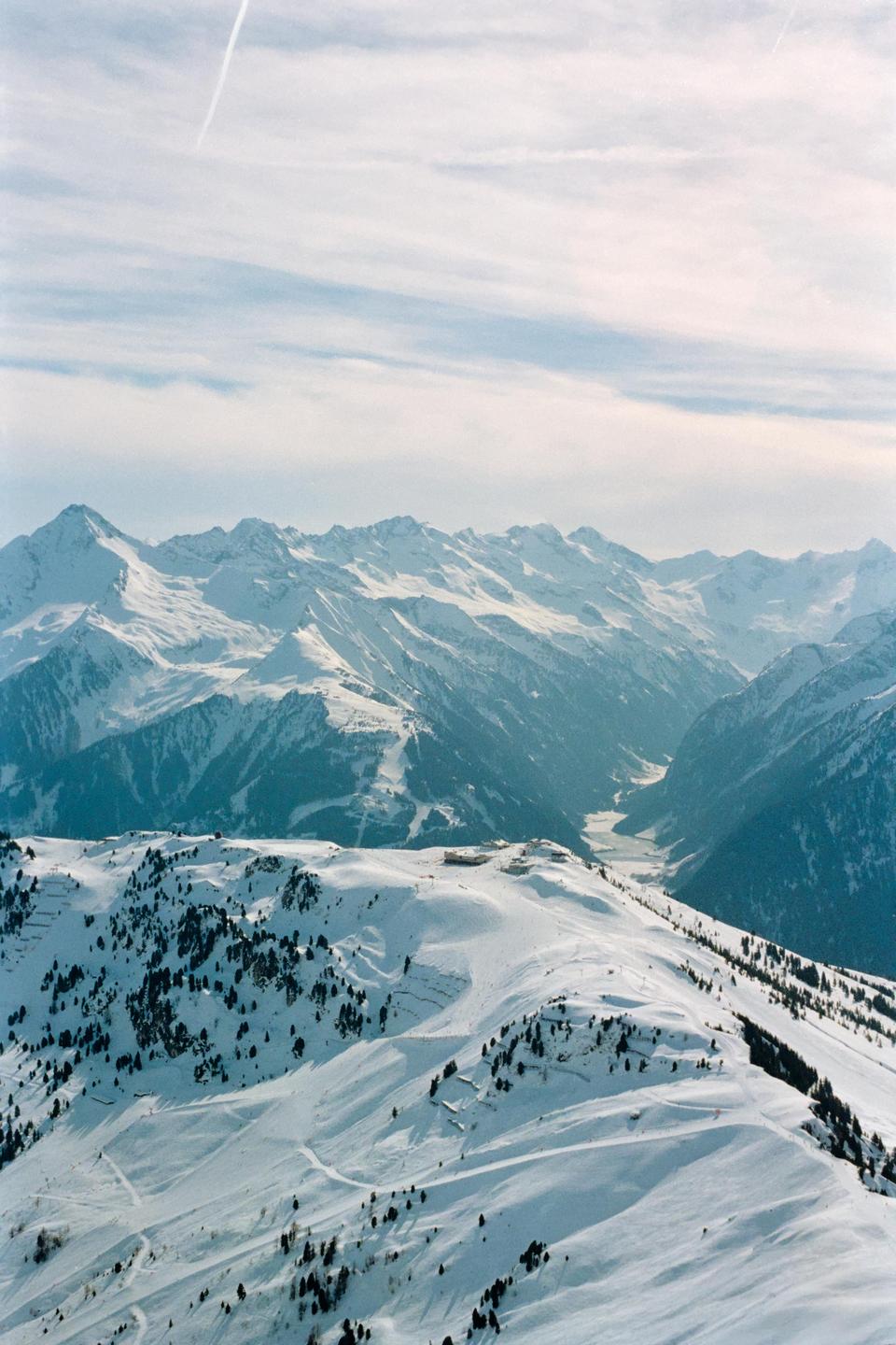 A vast mountain range covered in snow with a valley visible in the distance under a cloudy sky.