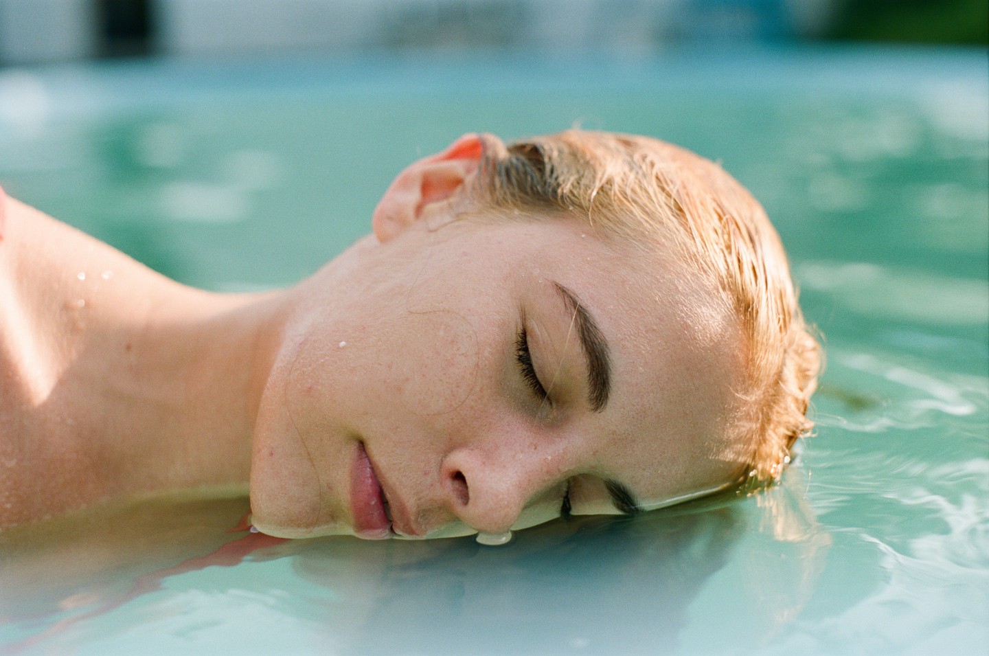 A woman with closed eyes floats in turquoise water.