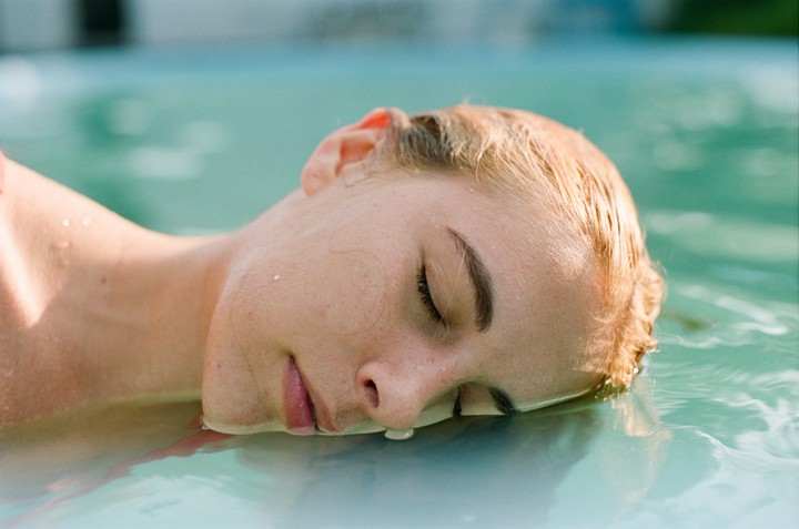 A woman with closed eyes floats in turquoise water.