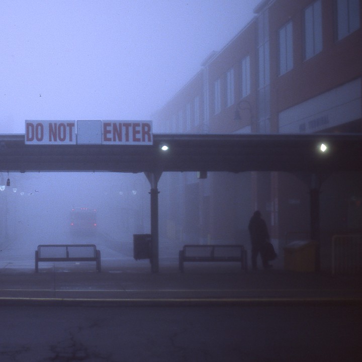 A person stands under a "DO NOT ENTER" sign at a bus terminal in the fog.