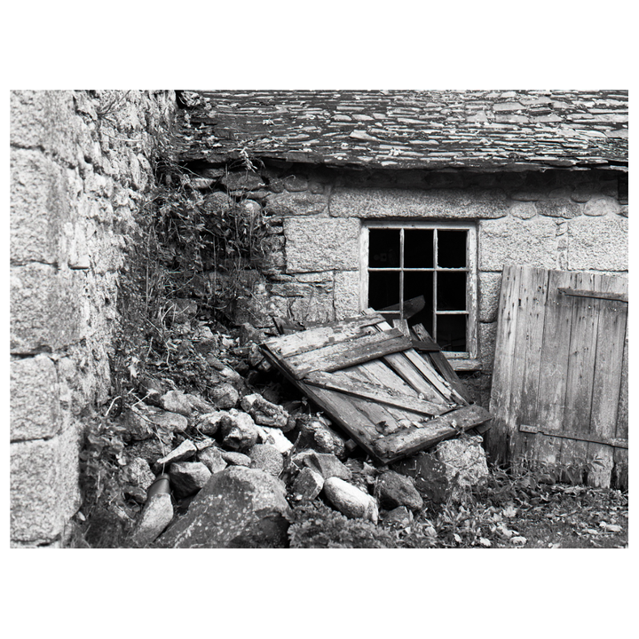 A stone building with a broken window and a pile of rubble in front of it is shown.