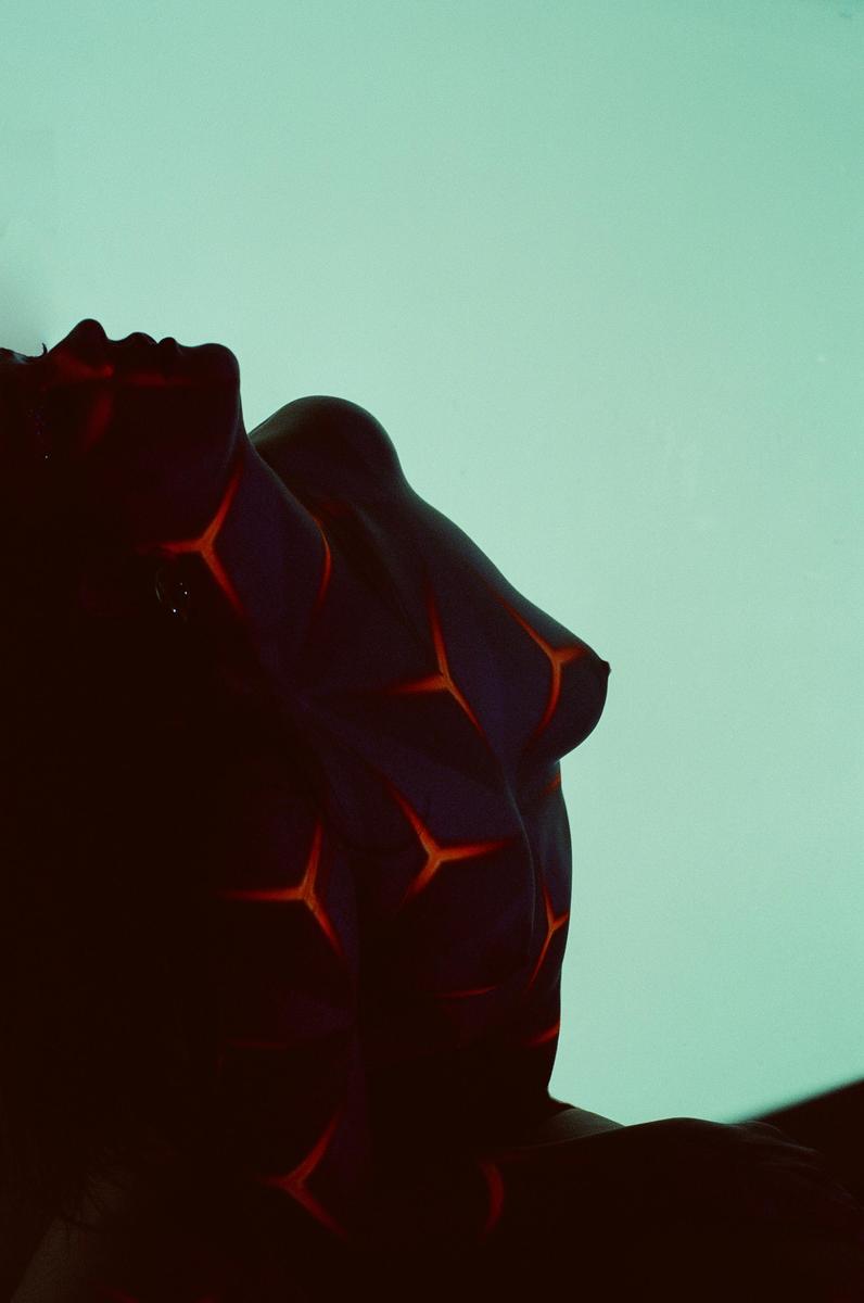 A woman with glowing orange patterns painted on her body is shown in profile against a light blue background.
