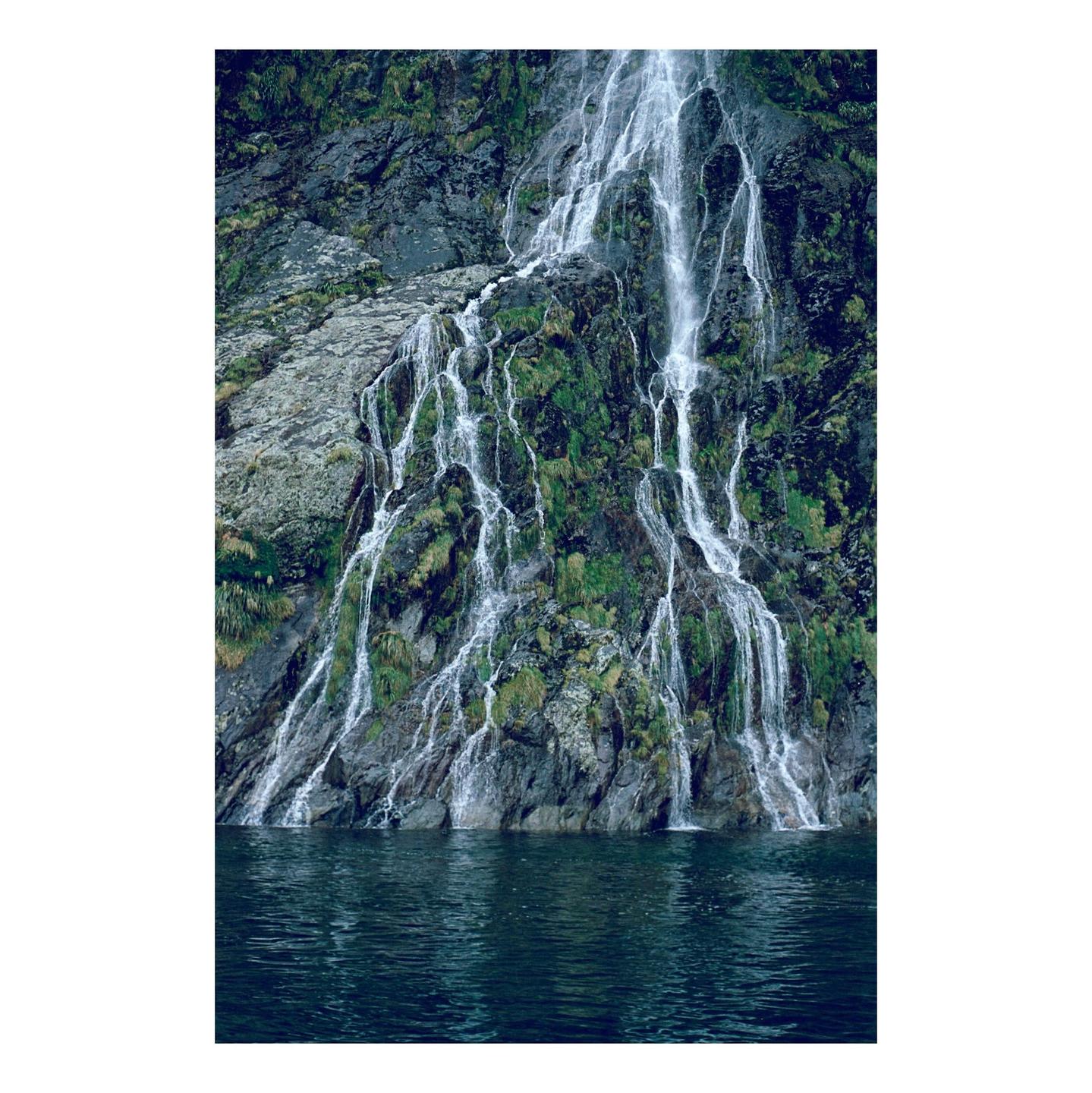 A waterfall cascades down a mossy rock face into a body of water.
