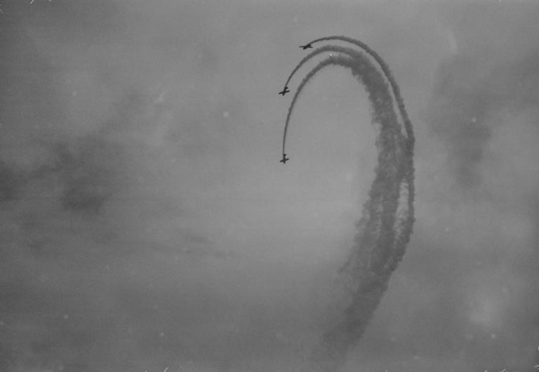 Three airplanes perform an aerial maneuver, leaving smoke trails in the sky.