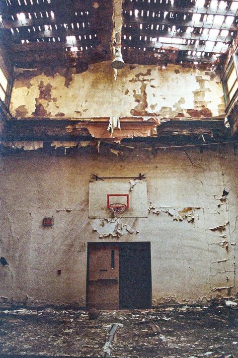 A basketball hoop is mounted on a wall with peeling paint in an abandoned school.