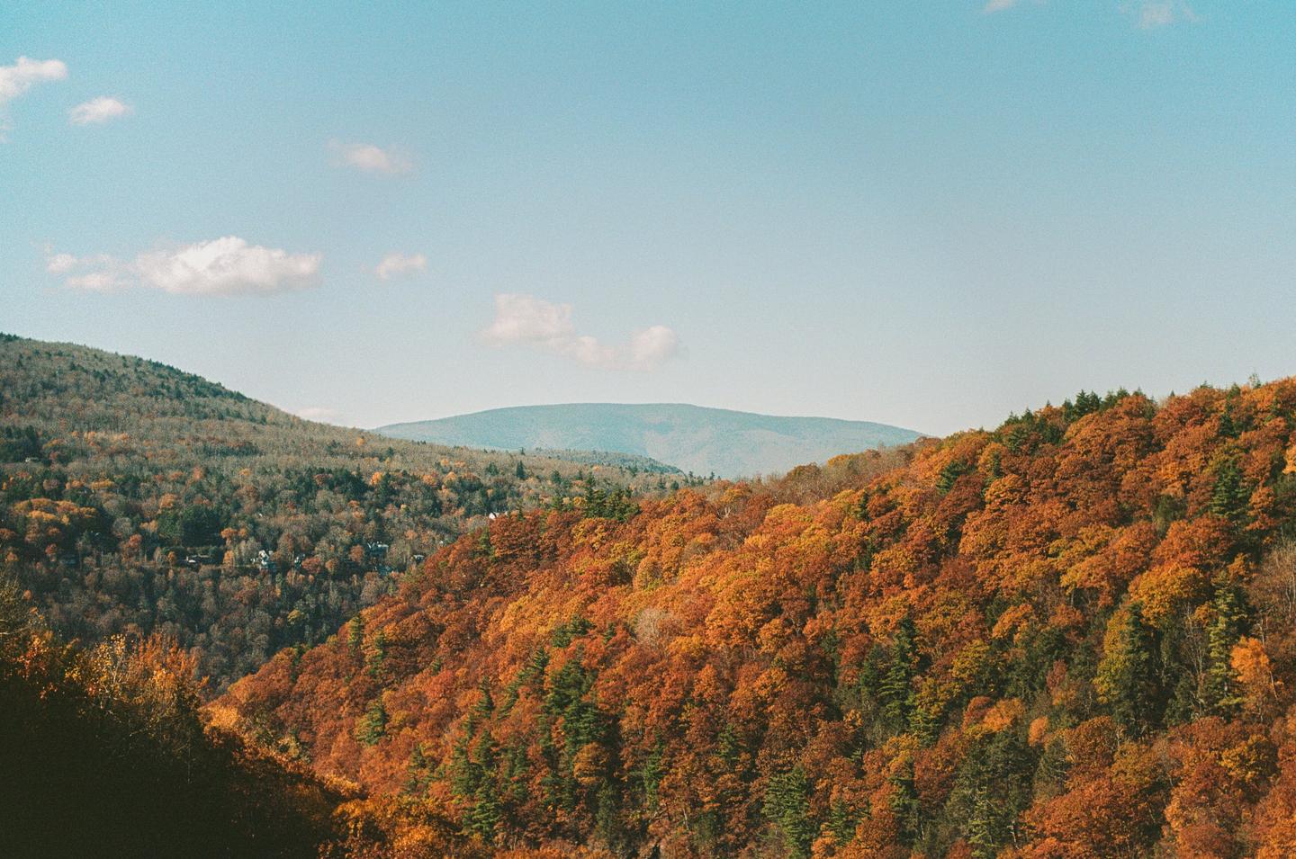A landscape view shows mountains covered in autumn foliage under a clear sky with a few clouds.