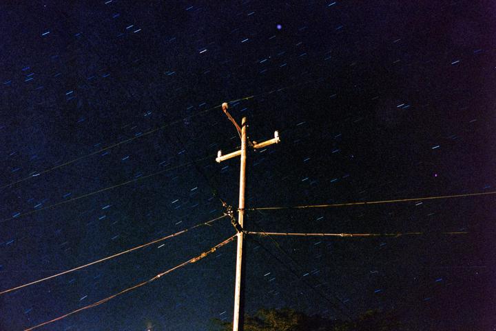A utility pole and power lines are visible against a night sky filled with star trails.