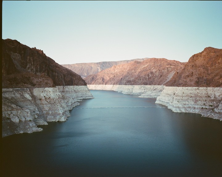 A wide shot shows a body of water surrounded by mountains with a clear sky.