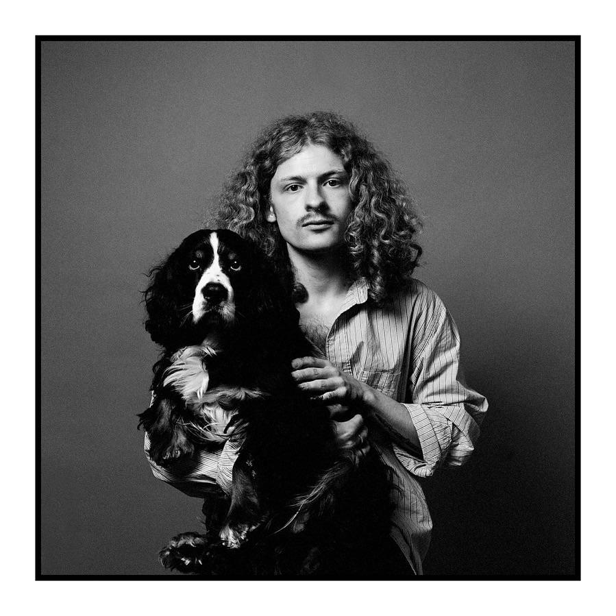 A man with curly hair and a mustache holds a spaniel.