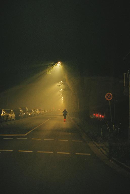 A person walks down a street at night, illuminated by streetlights and car headlights.