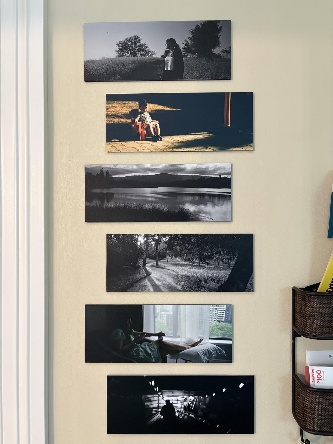 Six rectangular photographs are displayed vertically on a light-colored wall next to a white door frame.