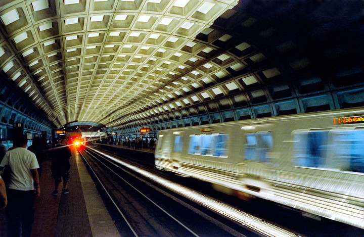 A subway train speeds through a station with a distinctive waffle-patterned ceiling.