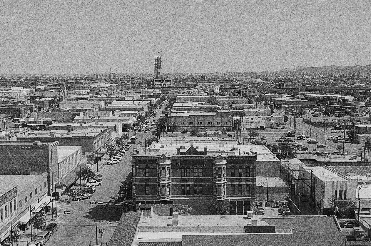 An elevated view shows a city with many buildings and streets with cars, with mountains in the distance.