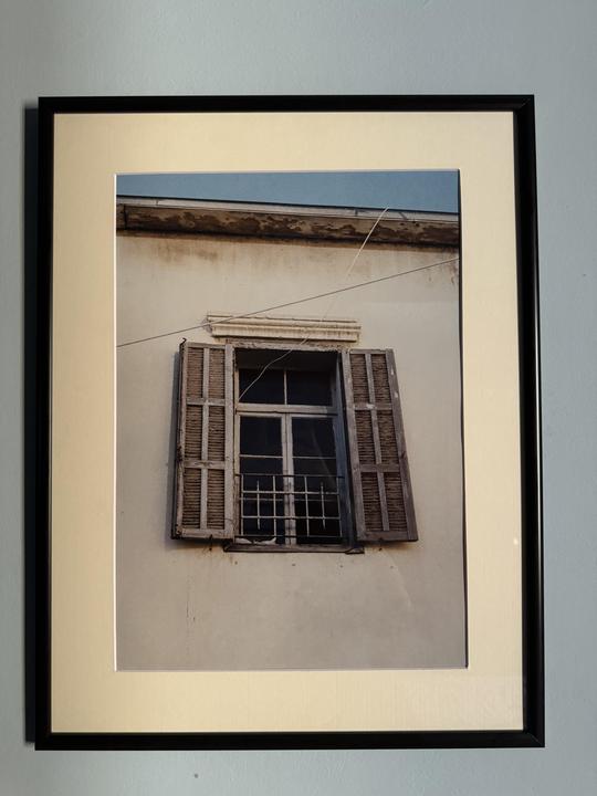 An old window with open wooden shutters and a metal grate is visible on a building facade.