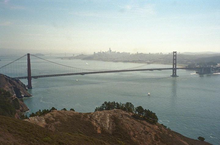 A wide shot shows the Golden Gate Bridge spanning a body of water with a city skyline in the distance.