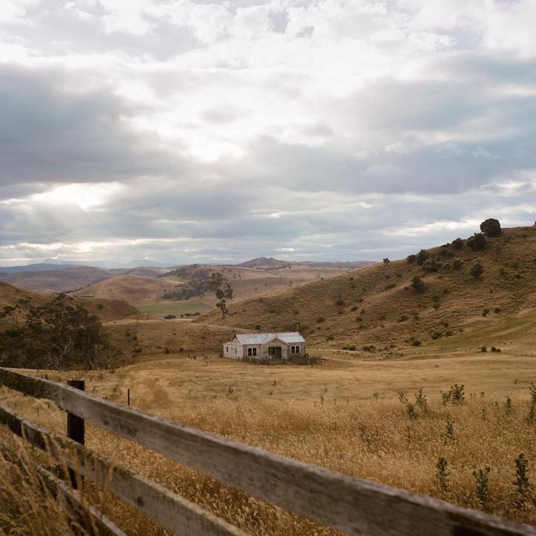 A farmhouse sits in a valley surrounded by rolling hills under a cloudy sky.
