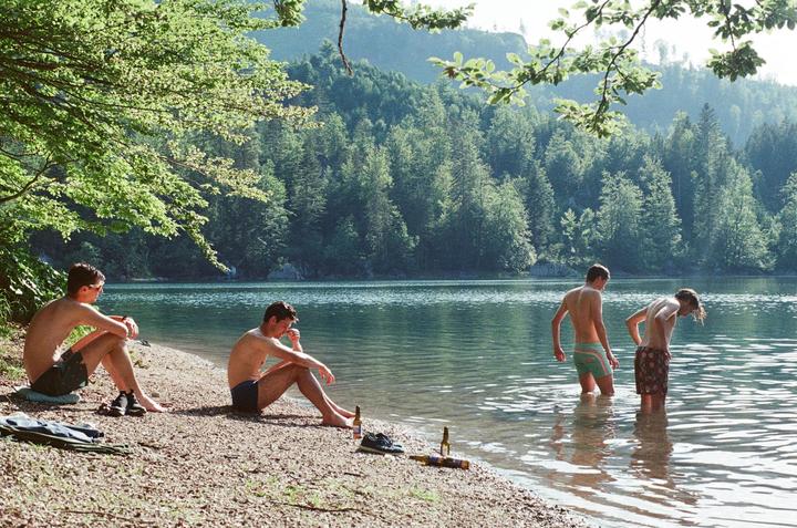 Four men are at the edge of a lake with a forest in the background.