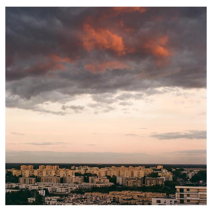 An aerial view shows a cityscape under a dramatic sky with dark clouds and a pink horizon.