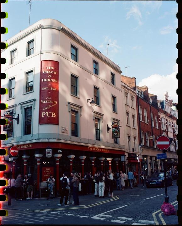 A crowd of people gathers outside The Coach & Horses pub on a street corner.