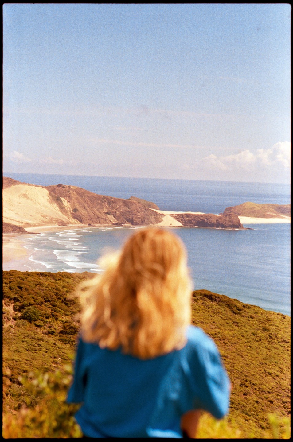 A woman with blonde hair looks out over a bay with sand dunes and hills.