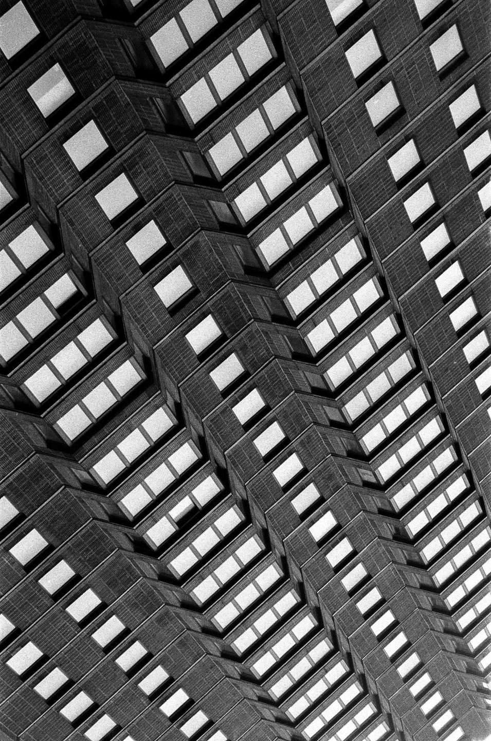 A black and white abstract architectural photograph shows a repeating pattern of windows and building facades.
