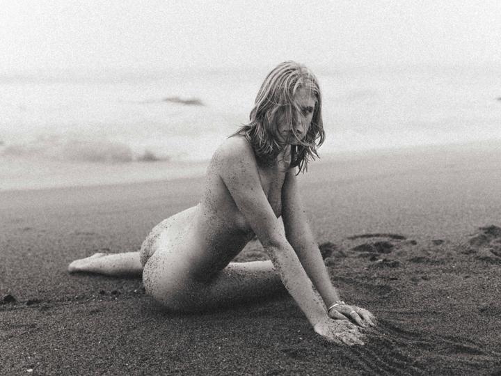 A woman covered in sand is kneeling on a beach.