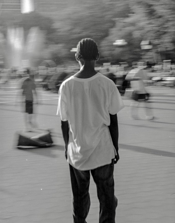 A boy stands with his back to the camera, looking at blurred figures in a street.