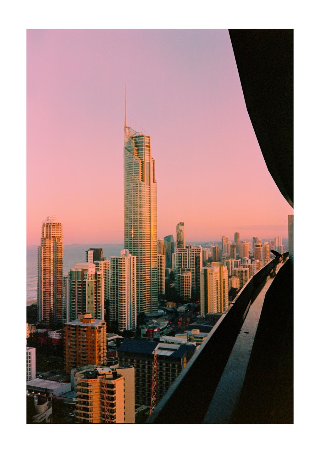 A city skyline with many tall buildings is visible from a high vantage point during sunset.