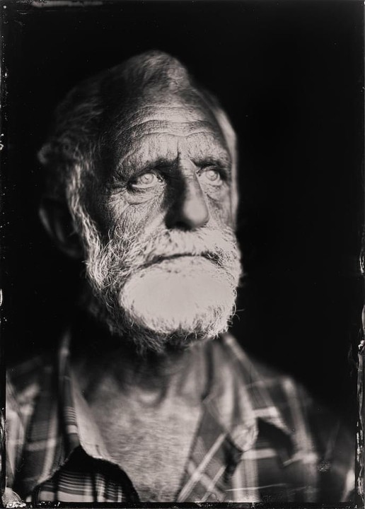 A man with a white beard and a plaid shirt looks up and to the right.