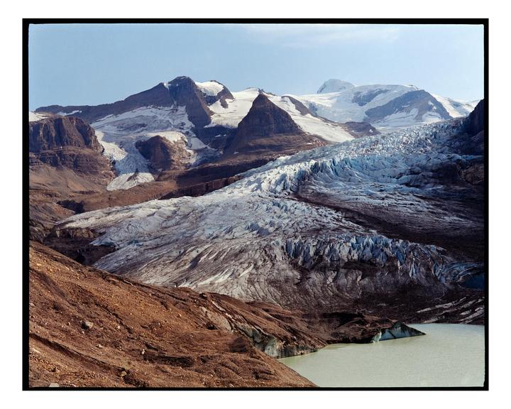 A large glacier flows down a mountain into a lake.