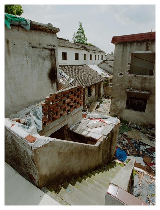 A narrow alleyway is surrounded by dilapidated buildings and debris.