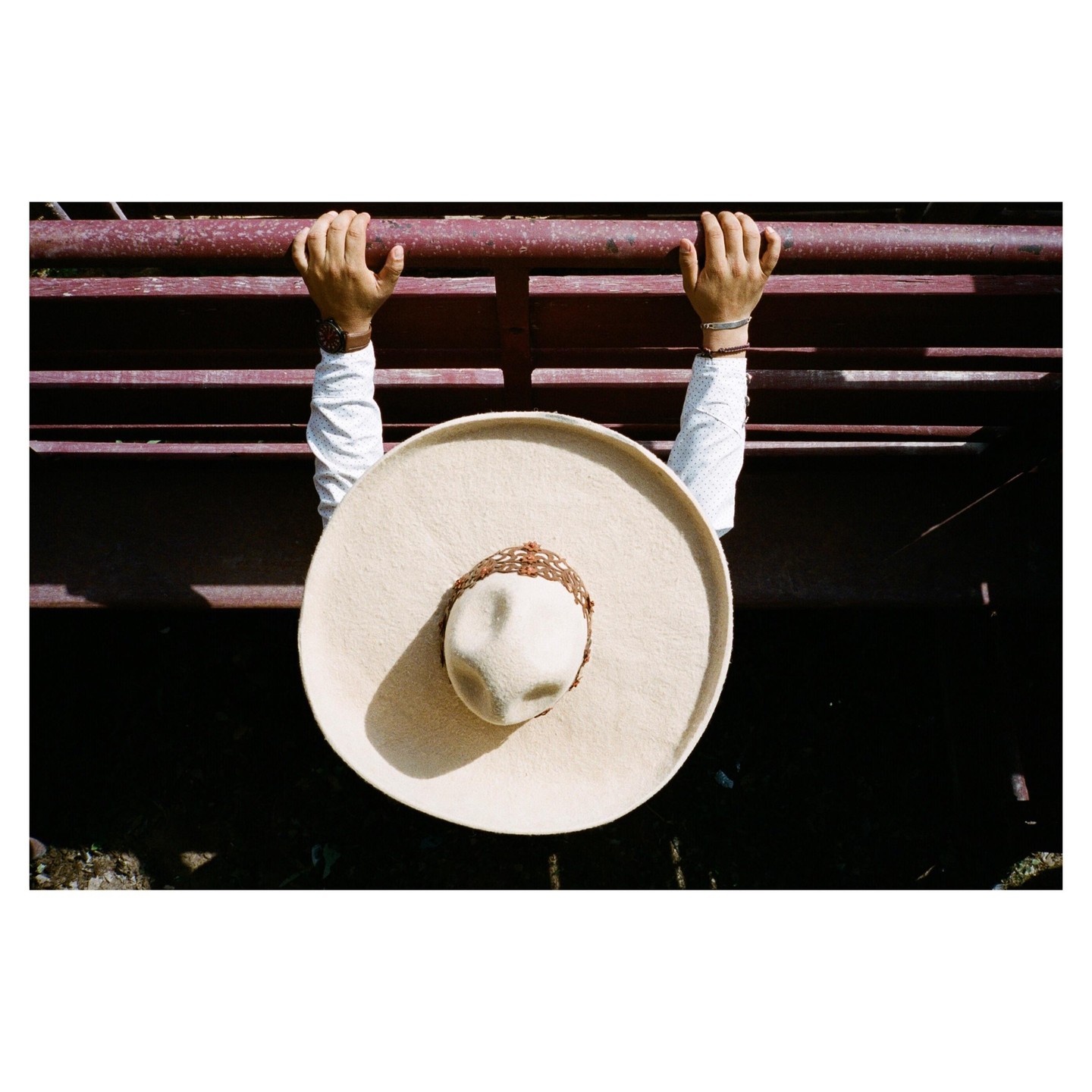 A person wearing a sombrero holds onto a red fence.