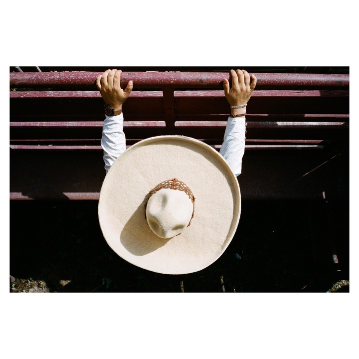 A person wearing a sombrero holds onto a red fence.