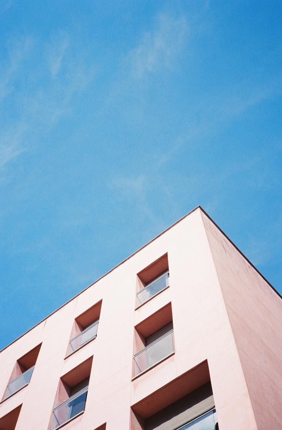 A pink building with multiple windows and balconies is photographed from a low angle against a clear blue sky.