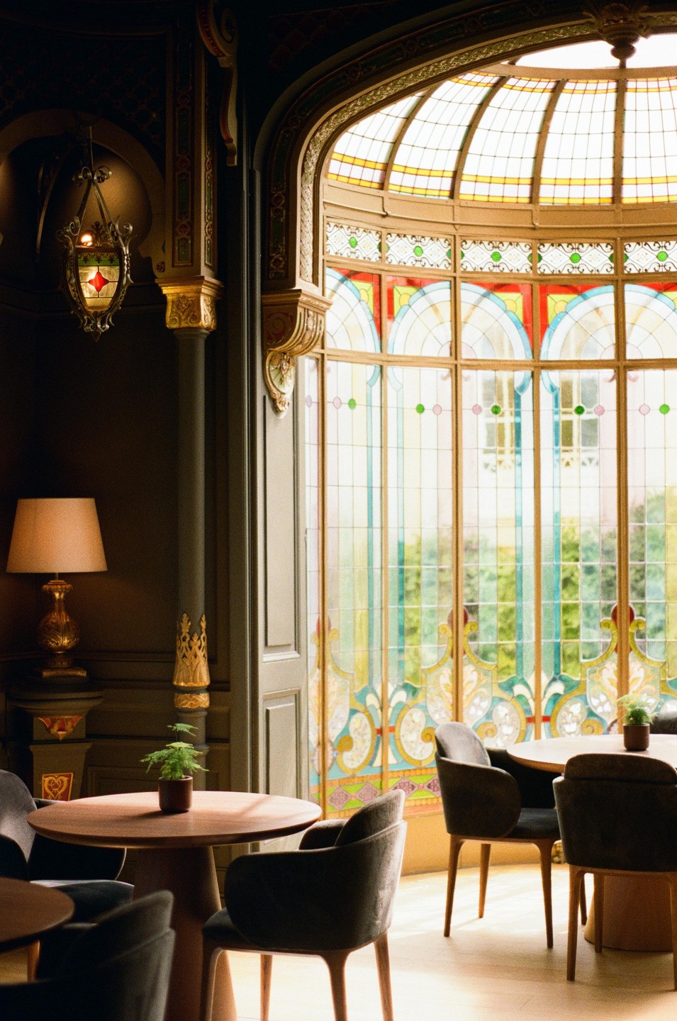 A room with ornate decor and stained glass windows features several tables and chairs.
