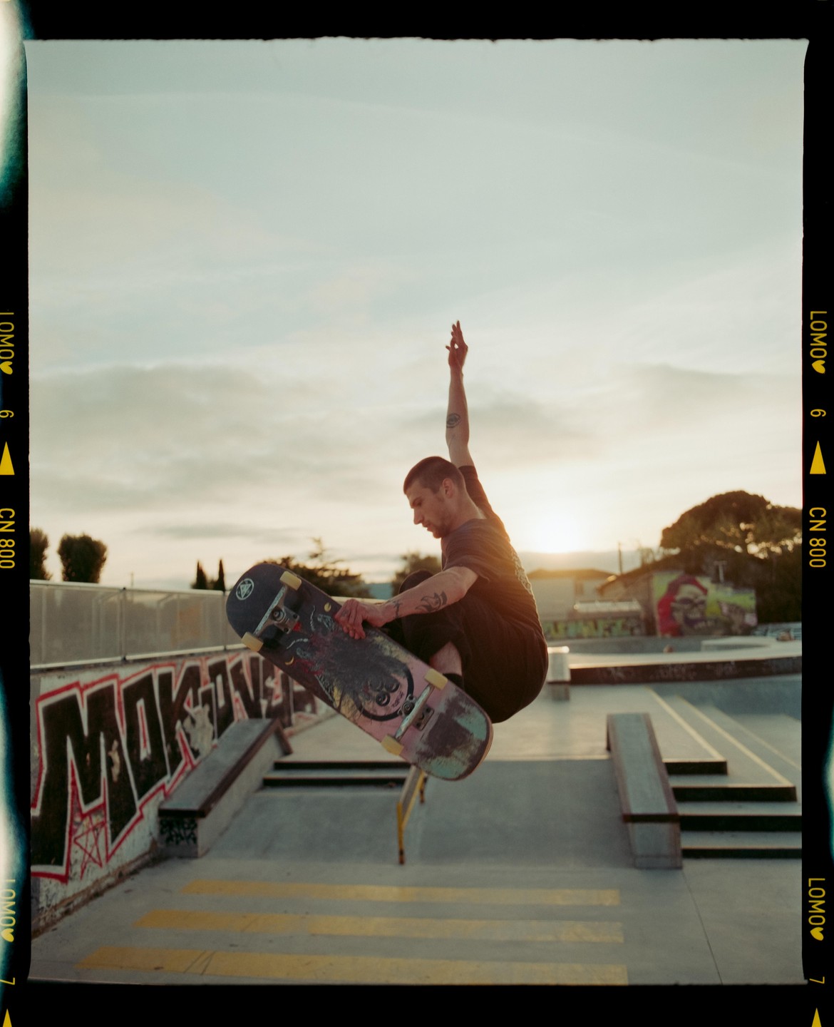 A man on a skateboard is captured mid-air at a skatepark during sunset.