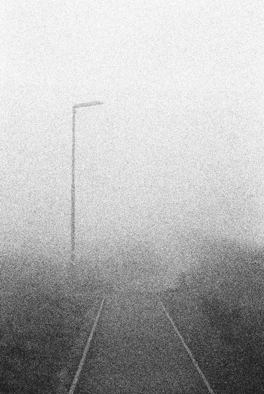 A single street light stands tall above a road disappearing into a thick fog.